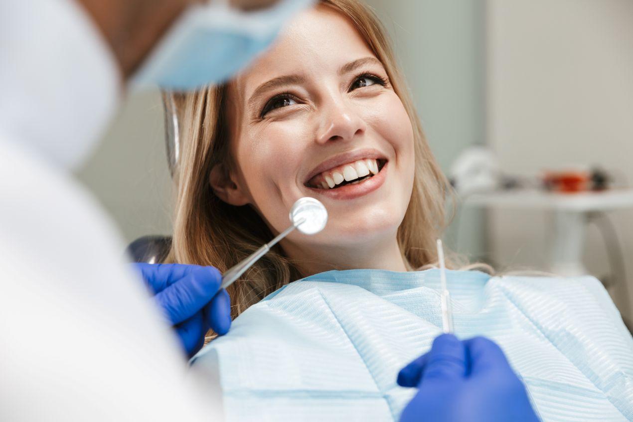 Zahnreinigung Essen: Junge Frau lacht während Untersuchung beim Zahnarzt mit Dentalspiegel